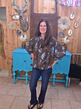 Load image into Gallery viewer, Someone standing wearing a rich brown top, with blue flowers. It has a 3/4" sleeve and buttons up.
